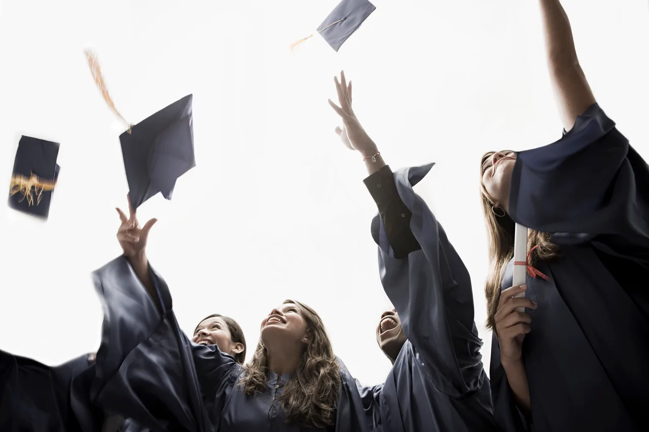 Happy graduates in black gowns throwing their caps high into the bright sky.